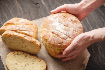 Female hands holding homemade natural fresh bread with a Golden crust on a napkin on an old wooden background