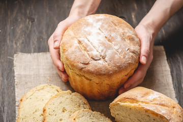 Female hands holding homemade natural fresh bread with a Golden crust on a napkin on an old wooden background
