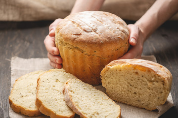 Female hands holding homemade natural fresh bread with a Golden crust on a napkin on an old wooden background