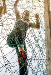 Female participant in an obstacle course climbing a net