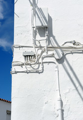 Fototapeta na wymiar Power supply cables. Connection boxes of telephony, cable TV and internet on the whitewashed wall of a village in southern Spain.