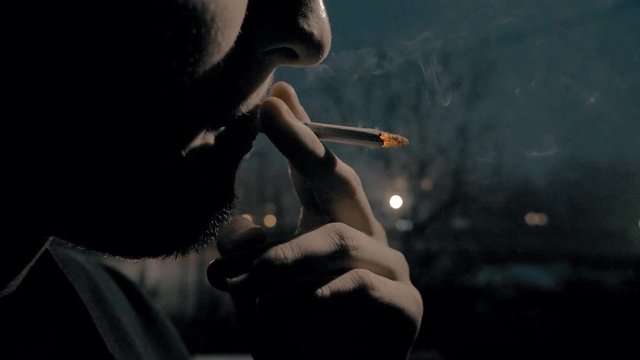 The guy smokes a cigarette, night, twilight, it rains.