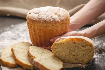Hands holding homemade natural fresh bread with a Golden crust on an old wooden background. Baking bakery products