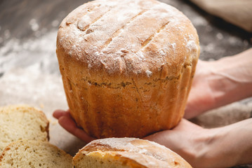 Hands holding homemade natural fresh bread with a Golden crust on an old wooden background. Baking bakery products
