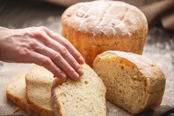 Women's hands breaking homemade natural fresh bread with a Golden crust on old wooden background. Baking bakery products