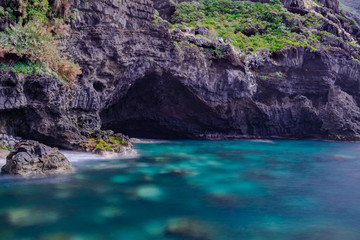 Fototapeta premium Cave eroded by the Atlantic ocean power, El Sauzal volcanic coastline, long exposure photography with sunlight, Tenerife, Canary islands, Spain