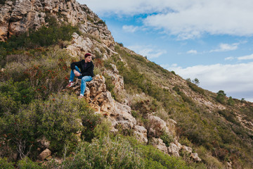 Fototapeta premium Young male sits on the rock and enjoys beautiful mountain landscape.