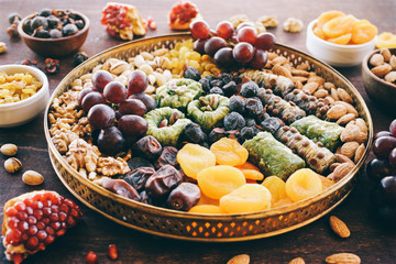 Middle East sweets, dry fruits and nuts on a copper tray. Top view, wooden background