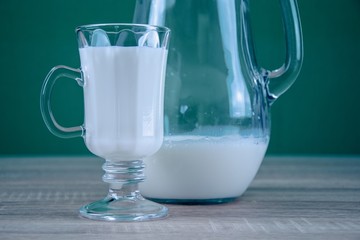Glass of milk standing on the table. Milk poured in a mug. Healthy food. Green background.