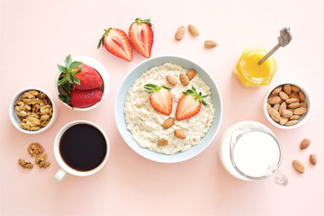 Oatmeal with honey, nuts and strawberries for breakfast. Light pink background. Flat lay