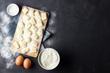 Raw uncooked homemade potato gnocchi with flour on cutting board. Top view. Dark background.