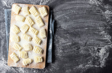 Raw uncooked homemade potato gnocchi with flour on cutting board. Top view. Dark background.