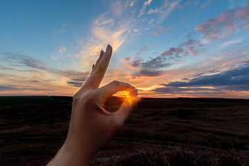 the space between the fingers of the hands at sunset. hand on sky background