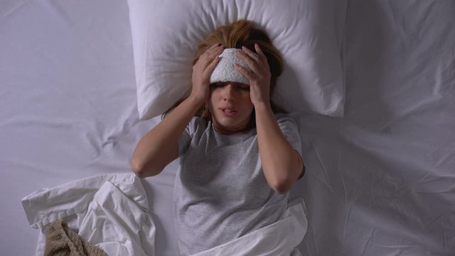 Sick woman putting compress on forehead to bring down temperature and headache