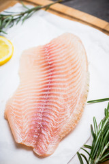 Raw tilapia fish fillet on the cutting board. Selective focus. Shallow depth of field.