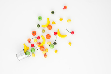 A scattering of many small different fruits on a white background. Mini copy of a metal bucket. The concept of diversity of flavors and additives. Multifruit.