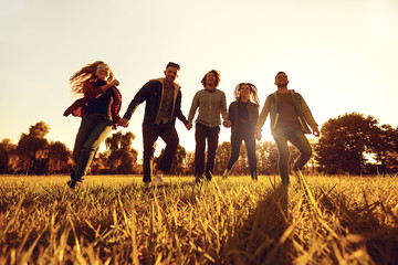A group of young people running through the grass in the park at sunset. 
