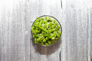 Frozen beans. Glass bowl with frozen green beans on beautiful wooden background