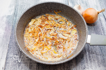 Fried onions in a pan. Cooking onions in a pan. Beautiful wooden background.