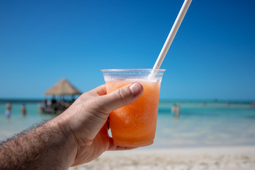 Close up of an orange & mango tropical cocktail overlooking a beautiful blurred beach setting background.