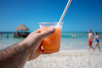 Close up of an orange & mango tropical cocktail overlooking a beautiful blurred beach setting background.