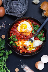 Fried eggs in tomato sauce with parsley and bread in a cast-iron pan. Shakshuka, typical Israel food. Breakfast or lunch. 