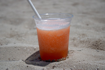 Close up of an orange & mango tropical cocktail overlooking a beautiful blurred beach setting background.