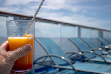 Close up of an orange & mango tropical cocktail overlooking a cruise ship blurred in the background.