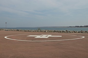Helipad on a pier near the sea with blue sky and clouds.