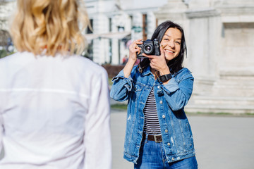 Professional female photographer with positive emotions taking photos of young pretty blond woman outdoors- private photo session in city street concept outdoors.