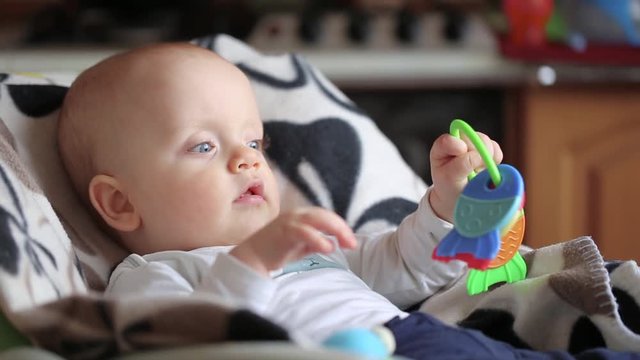 baby boy nibbles a teether toy. the child is sitting on the highchair. face close up