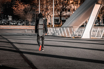 Young teenage skater walking on an industrial footbridge. Tactical extreme back pack with board strapped on. Going to a race. 