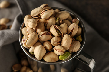 Mug with tasty pistachio nuts on table, closeup