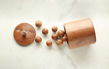 Wooden jar with tasty macadamia nuts on light background
