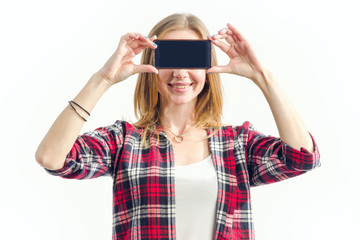Close up portrait blonde woman is holding a smartphone in hands in front of face. Showing blank screen mobile phone. Girl closed eyes phone standing on light background. Innovations technology.