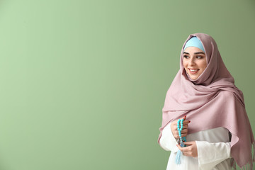 Muslim woman with tasbih on color background