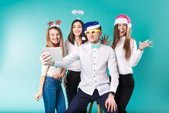 New Year Theme Christmas Winter Office Company Employees. Group 4 Young Caucasian People Business Smile Holiday Funny Hats Accessories Glasses Take Photo Yourself Selfie Tablet Blued Background