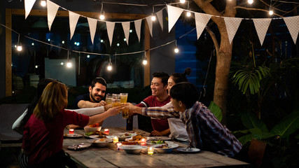 Asian group eating and drinking cold beer outside the house at night, having fun talking