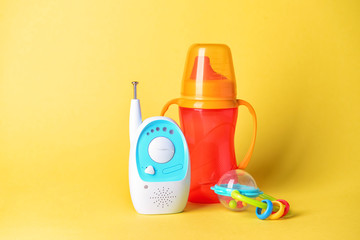 Modern baby monitor with toy and bottle on color background