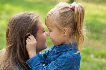 little happy girl hugs her mom and tells her something in the ear in the park