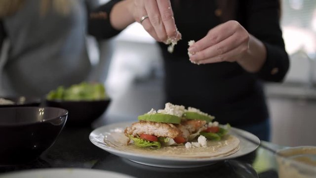 Close up of woman&rsquo;s hands crumbling feta cheese on top of a healthy tortilla wrap