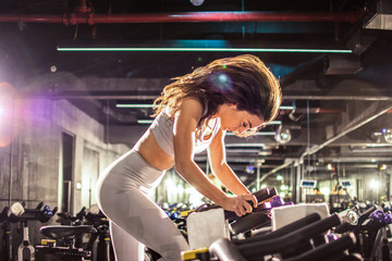 Fototapeta na wymiar Side shot of attractive young brunette sportswoman riding exercise bike during cycling workout in gym