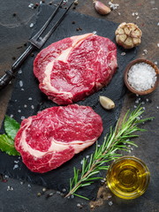 Raw  Rib eye steak or beef steak on the graphite board with herbs and spices.