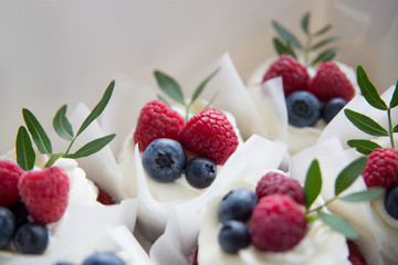 Appetizing cupcakes with white cream, raspberries and blueberries decorated with green leaves.