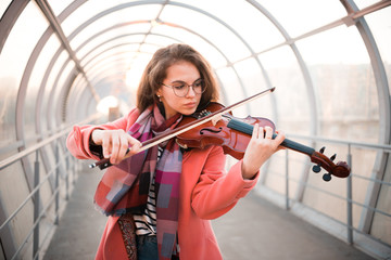 Young woman in glasses playing a fiddle on the overhead passage