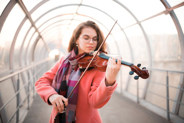 Inspired young woman in glasses playing a fiddle on the overhead passage