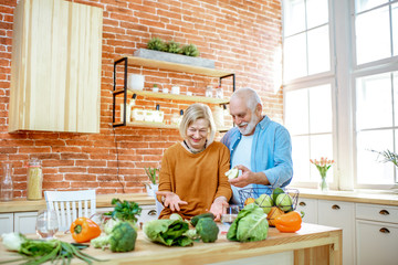 Cheerful senior couple eating fruits standing together with healthy food on the kitchen at home. Concept of healthy nutrition in older age