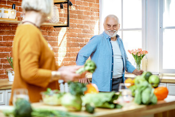 Fototapeta premium Cheerful senior couple cooking food with healthy fresh ingredients on the kitchen at home. Concept of healthy nutrition in older age