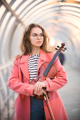 Young woman in glasses standing on the upper pedestrian crossing holding a violin