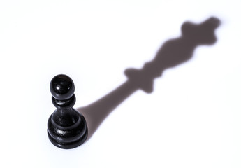 Black chess pawn with queen shadow on white background. Conceptual picture - dreaming and...